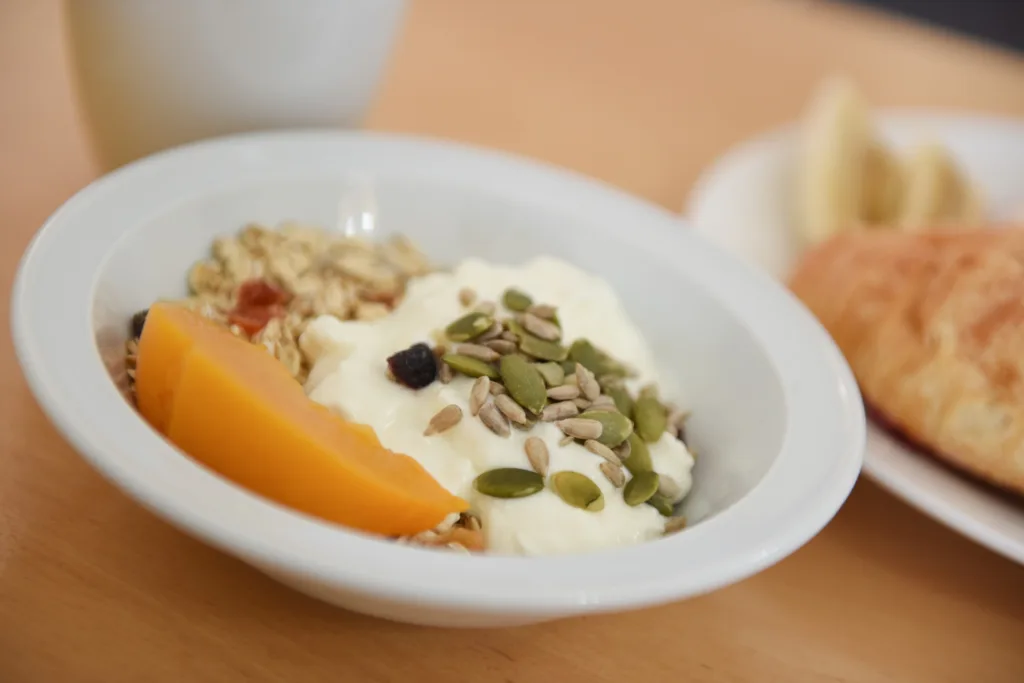 Muesli with yoghurt, peach slices and seeds, with a croissant alongside