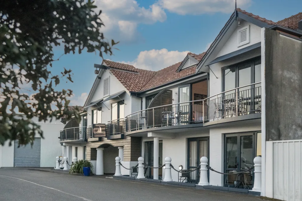 Harbourside Nelson marina-front building with balconies, white bollards and sail logo sign