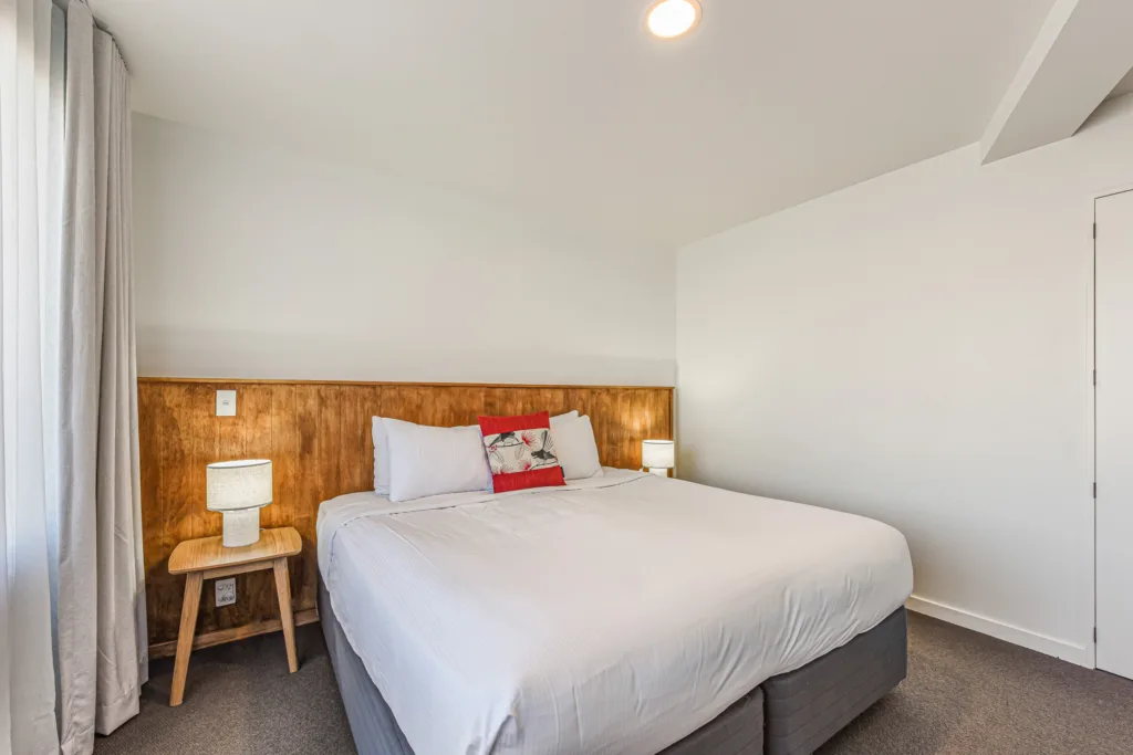 Marina Front Apartment bedroom with super king bed, timber headboard wall and bedside lamps